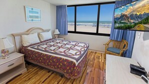 A bedroom with a bed, a chair, a desk, and a large window with a beach view.