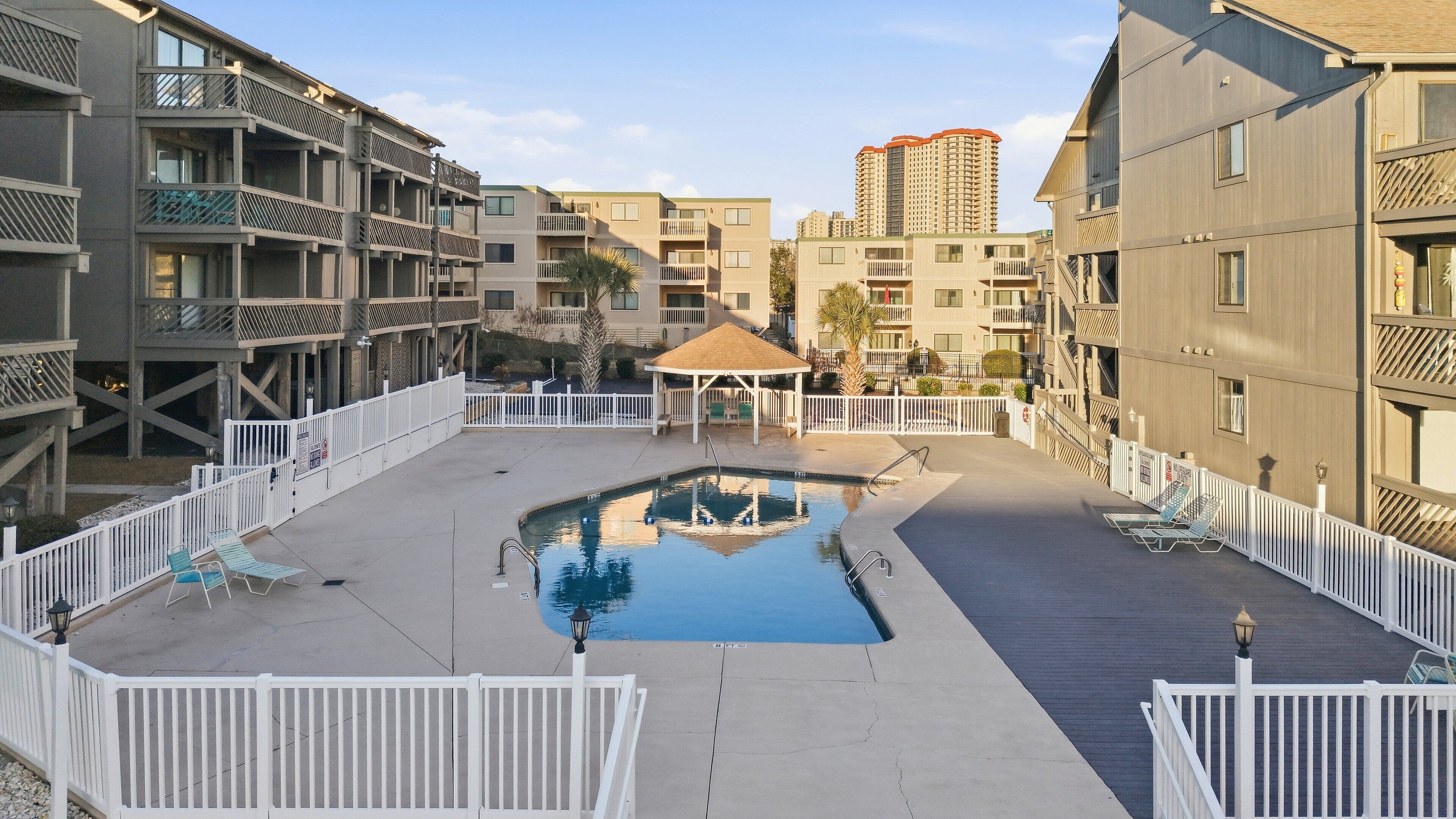A pool area with a gazebo, white railings, and a view of surrounding buildings.
