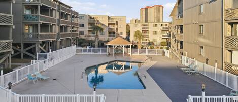 A pool area with a gazebo, white railings, and a view of surrounding buildings.