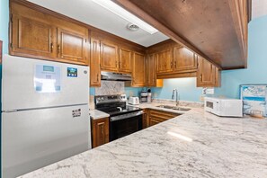 A kitchen with wooden cabinets, a stainless steel refrigerator, a stove, and a microwave. - Shipwatch Pointe II N104 (Myrtle Beach)