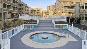 A pool area with a central hot tub, surrounded by a deck with lounge chairs and a staircase leading to upper floors. - Shipwatch Pointe II N104 (Myrtle Beach)