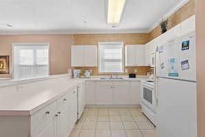 A kitchen with white cabinets, a double sink, a refrigerator, and a window with blinds.
