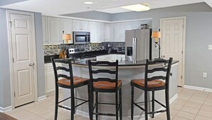 Una cocina con armarios blancos, una isla central con taburetes de bar, un refrigerador, microondas y estufa.