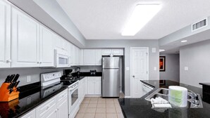 Una cocina moderna con armarios blancos, electrodomésticos de acero inoxidable, encimera negra y piso de baldosas.