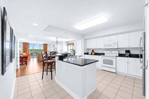 A modern kitchen with white cabinets, a central island, and a dining area with a view. - Yacht Club 2-505 - Three Bedroom (North Myrtle Beach)
