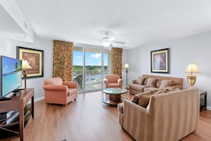 A modern living room with a sofa, armchairs, a coffee table, and a TV. There are curtains and a ceiling fan. - Yacht Club 2-505 - Three Bedroom (North Myrtle Beach)