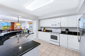 A modern kitchen with white cabinets, a black countertop, stainless steel appliances, and a view of the outdoors.