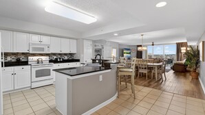 A spacious kitchen with white cabinets, a central island, and a dining area with a view. - Yacht Club 2-802 - North Myrtle Beach (North Myrtle Beach)