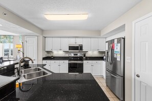 A modern kitchen with white cabinets, a stainless steel refrigerator, a microwave, and a black granite countertop.