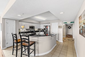 A modern kitchen with white cabinets, a central island, and a dining area with wooden chairs.