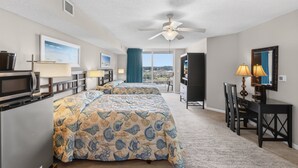 A hotel room with a bed, a desk, a chair, a TV, a microwave, a ceiling fan, and a view of the outside.