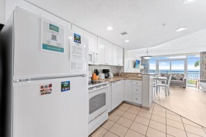 A modern kitchen with white cabinets, a built-in oven, and a dining area with a view of the ocean. - Atlantica 154, Beachfront Myrtle Beach Sping Retreat (Myrtle Beach)