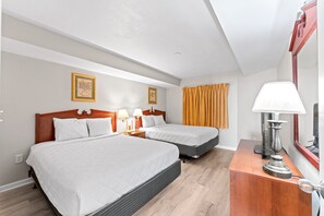 A hotel room with two beds, a wooden nightstand, a lamp, and a mirror.