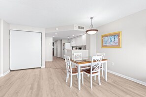 A modern kitchen with white cabinets, a dining table with white chairs, and a pendant light. - Atlantica 154, Beachfront Myrtle Beach Sping Retreat (Myrtle Beach)