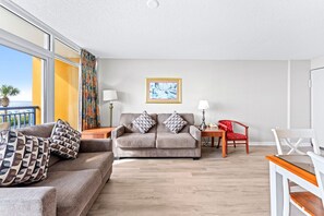 A living room with a sofa, a red chair, a small table with a lamp, and a painting on the wall. - Atlantica 154, Beachfront Myrtle Beach Sping Retreat (Myrtle Beach)