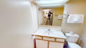 Un baño con lavamanos, espejo e inodoro. Se observa un trípode de cámara al fondo.