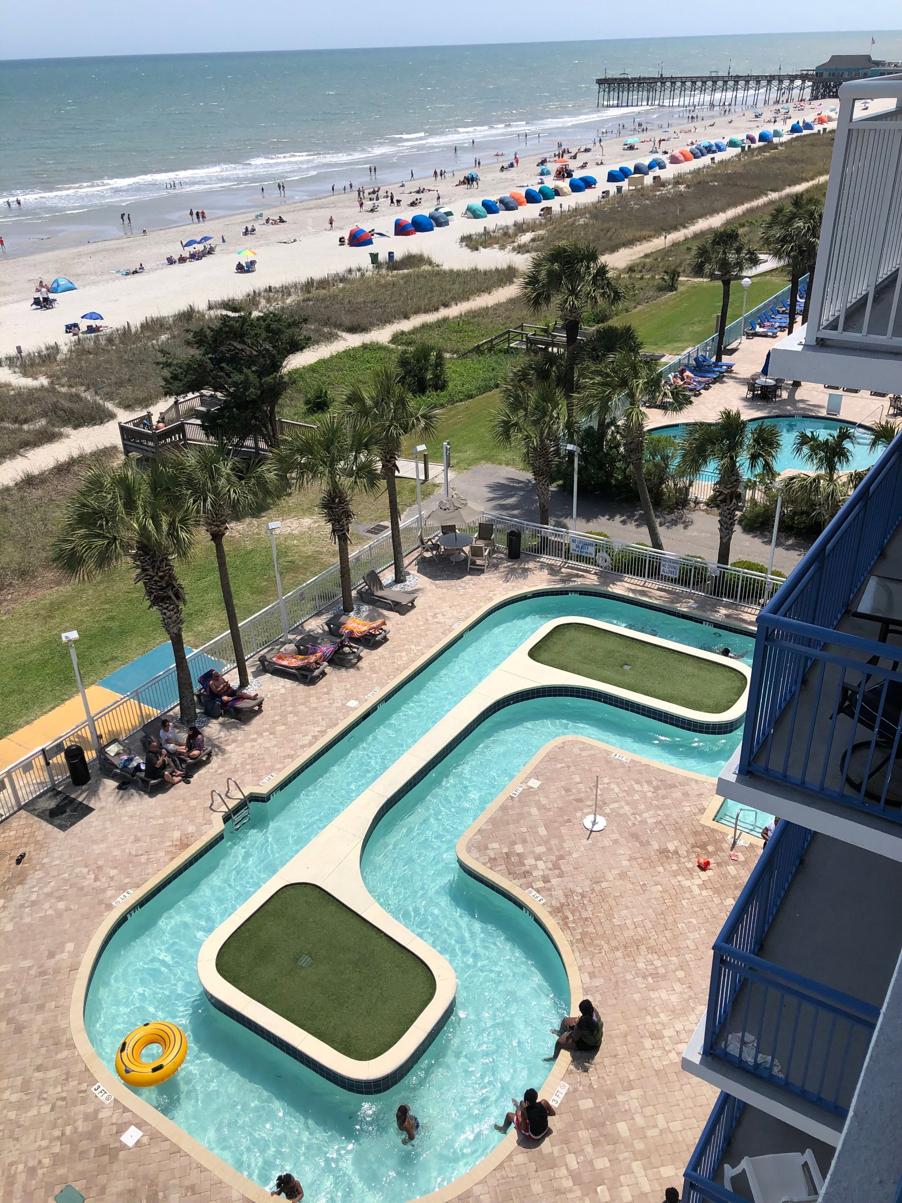 Un espace piscine comprenant plusieurs piscines, une plage avec des parasols et une jetée en arrière-plan.