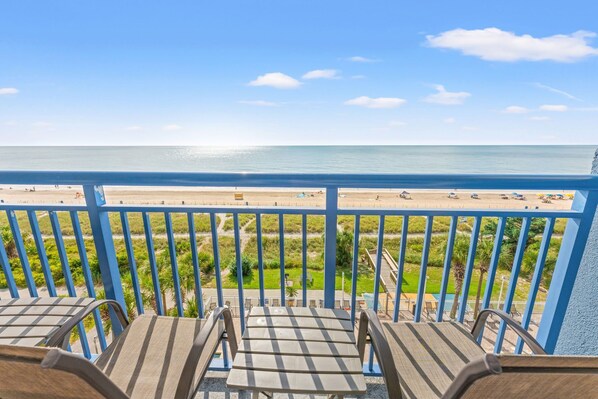 A balcony with a view of a beach, featuring a railing and several chairs.