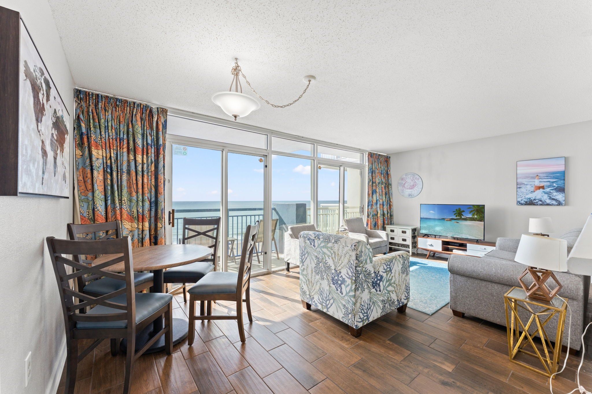 A modern living room with a dining area, a television, and a balcony with a view of the sea.
