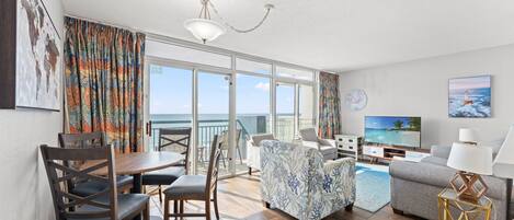 Un salon moderne comprenant un coin repas, un téléviseur et un balcon avec vue sur la mer.