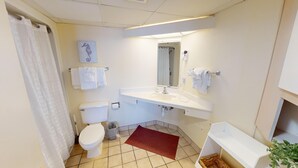 A small, clean bathroom with a toilet, sink, and shower. There is a towel rack, a mirror, and a small trash bin.