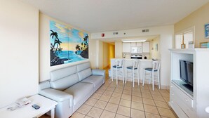 A compact living space with a kitchenette, a dining area with white chairs, a sofa, and a TV.