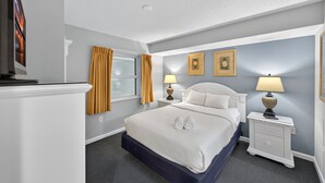 Une chambre d’hôtel avec un lit, deux tables de chevet avec des lampes, une télévision et deux tableaux encadrés au mur.