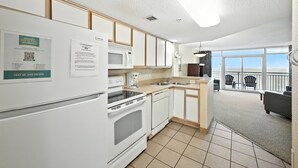 A modern kitchen with white appliances, a dining area with a view, and a balcony with chairs. - Atlantica 754, Beachfront Charm, Oceanfront Views, Beach Escape (Myrtle Beach)