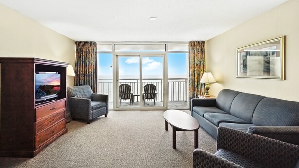 A hotel room with a balcony, a TV, a sofa, a chair, and a lamp. - Atlantica 754, Beachfront Charm, Oceanfront Views, Beach Escape (Myrtle Beach)