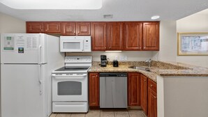 A kitchen with wooden cabinets, a white refrigerator, a microwave, an oven, a dishwasher, and granite countertops. - Atlantica 854, Oceanfront | Myrtle Beach Serenity Condo (Myrtle Beach)