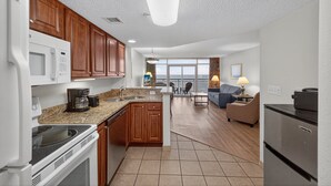 A modern kitchen with granite countertops, wooden cabinets, and stainless steel appliances. There is a dining area with a view of the ocean. - Atlantica 854, Oceanfront | Myrtle Beach Serenity Condo (Myrtle Beach)