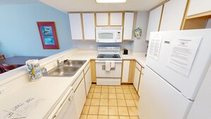 A compact kitchen with white appliances, a tiled floor, and a framed picture on the wall.