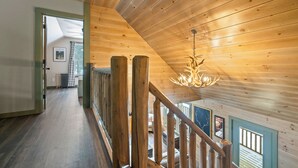 A wooden interior with a staircase, a chandelier, and a view of the outdoors. - Red Fox Lodge - Close to downtown Rangeley w/ Hot Tub & Sauna (Rangeley)