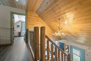 A wooden interior with a staircase, a chandelier, and a view of the outdoors.