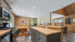 A modern kitchen with wooden cabinetry, a central island, and built-in appliances. - Red Fox Lodge - Close to downtown Rangeley w/ Hot Tub & Sauna (Rangeley)