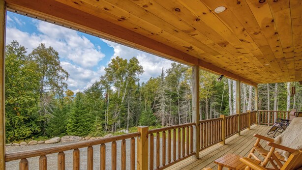A wooden deck with a railing, outdoor furniture, and a view of a forested area. - Red Fox Lodge - Close to downtown Rangeley w/ Hot Tub & Sauna (Rangeley)