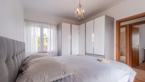 Ein Schlafzimmer mit einem großen Bett, einer Chandelüster und Blick ins Freie.