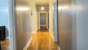 A hallway with wooden flooring, white walls, and a ceiling vent.