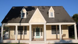 A two-story house with a front porch, a central door, and two small windows on the second floor.