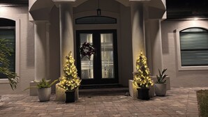 Un bâtiment avec une entrée sombre, deux sapins de Noël illuminés et une couronne accrochée à la porte.