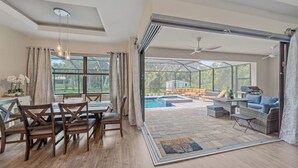 Un espace intérieur spacieux comprenant une table à manger et des chaises, ainsi qu’une grande porte-fenêtre coulissante donnant sur une terrasse extérieure avec une piscine et un coin salon.