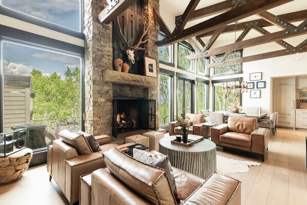 A spacious living area with a stone fireplace, leather sofas, and large windows offering a view of the outdoors.