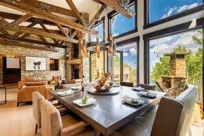 Un vaste espace dédié à la salle à manger, avec une grande table, des sièges confortables, une cheminée en pierre et une vue sur l’extérieur.