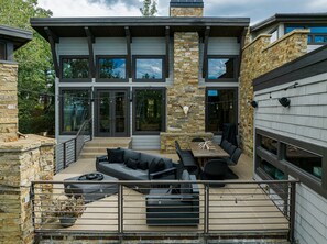 Ein modernes Haus mit Natursteinfassade, großen Fenstern und einer Außenveranda mit Möbeln.