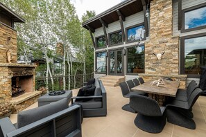 A modern outdoor patio with a stone fireplace, outdoor seating, and a view of the house.
