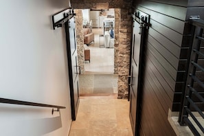 Un couloir étroit avec un mur en pierre, une porte en bois et une vue sur un espace de vie comprenant un canapé et une table.