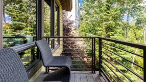 Ein Balkon mit Korbstühlen, einer Holzterrasse und Blick auf Bäume sowie ein Gebäude.