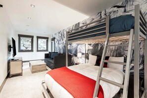 Une chambre avec un lit superposé, une couverture rouge, un bureau, une chaise et un téléviseur.