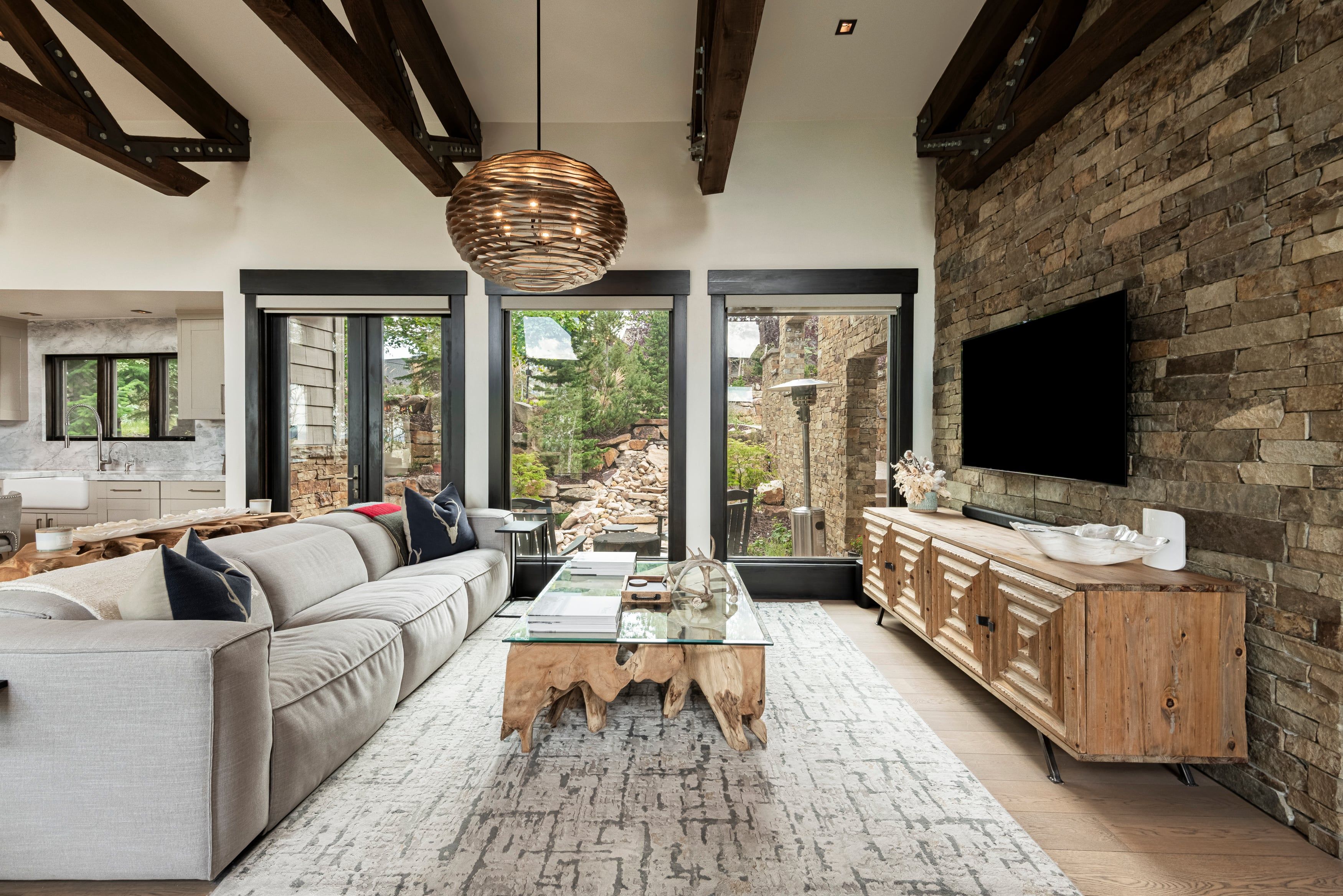 A modern living room with a sofa, coffee table, and a TV on a stone wall.