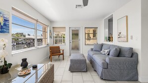 Un amplio espacio de sala con un ventanal grande, un sofá, una silla y una pequeña mesa con un florero y un plato de comida.